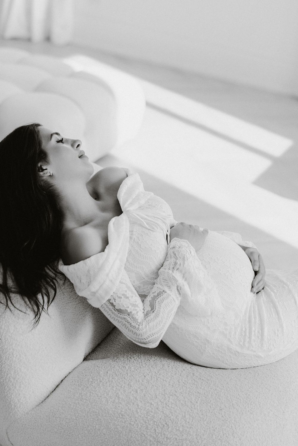 Expectant mother reclining in soft light, black and white.