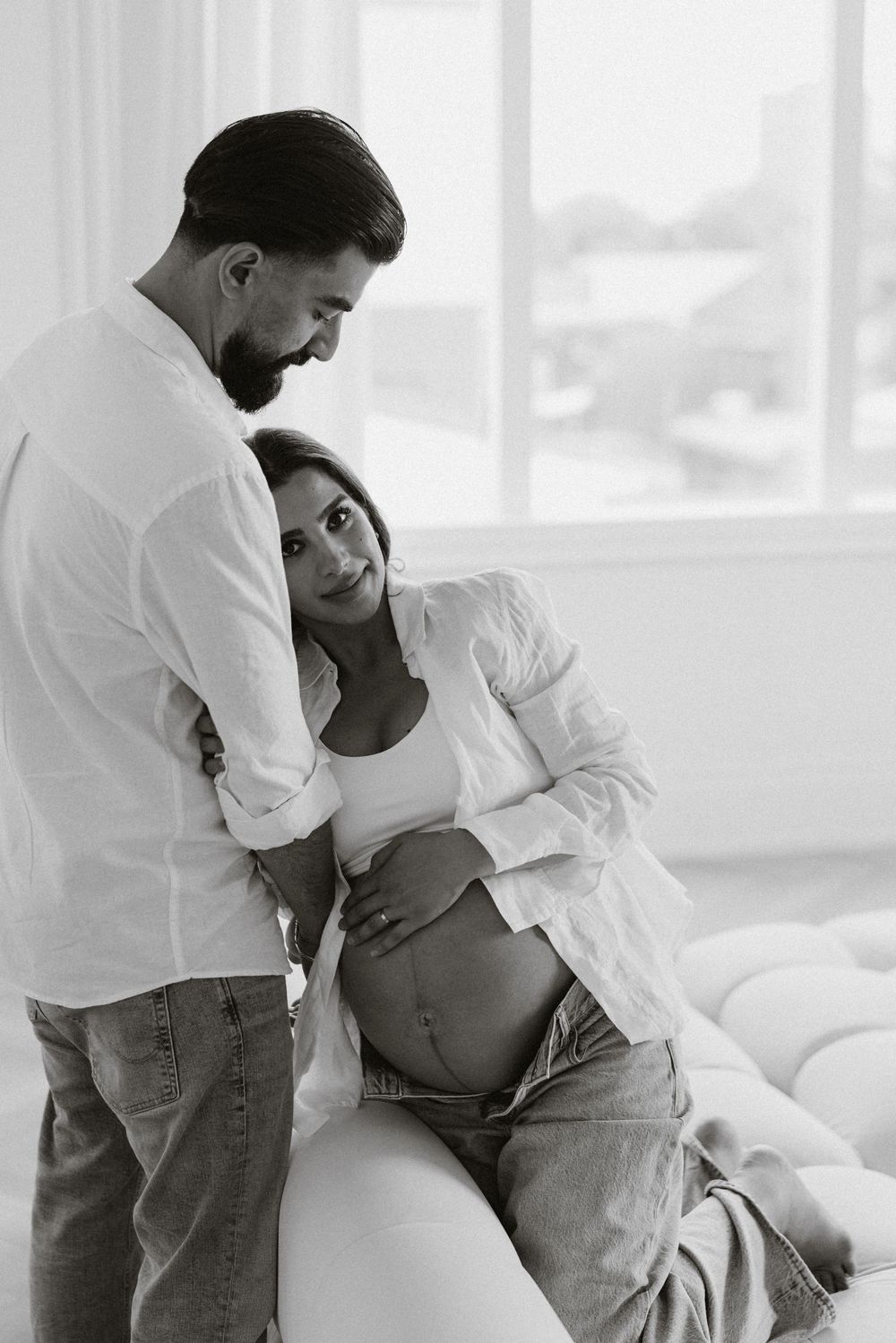 Partner leaning over the expectant mother by the window.