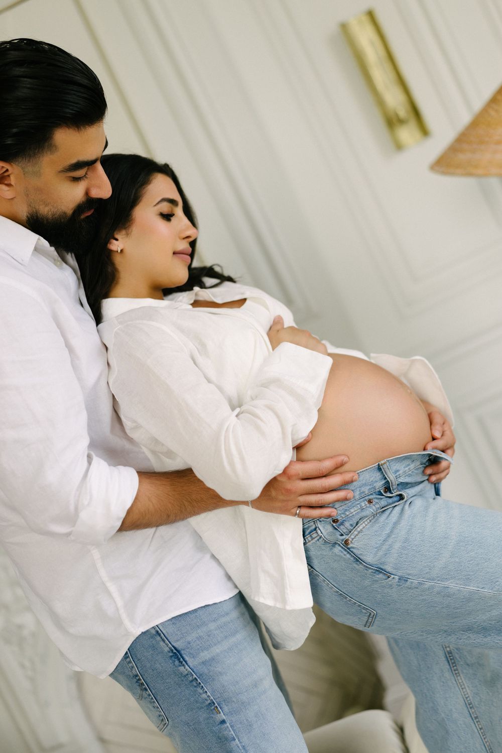 Partner embracing the expectant mother in a white shirt and jeans.
