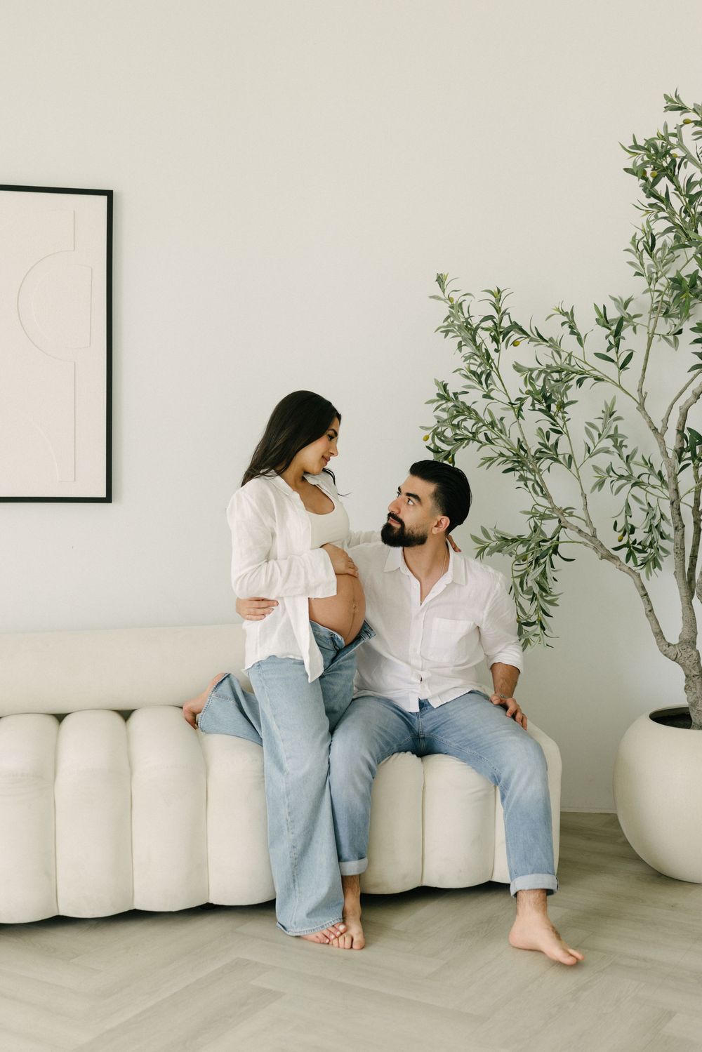 Expectant couple seated together in a minimalist studio.