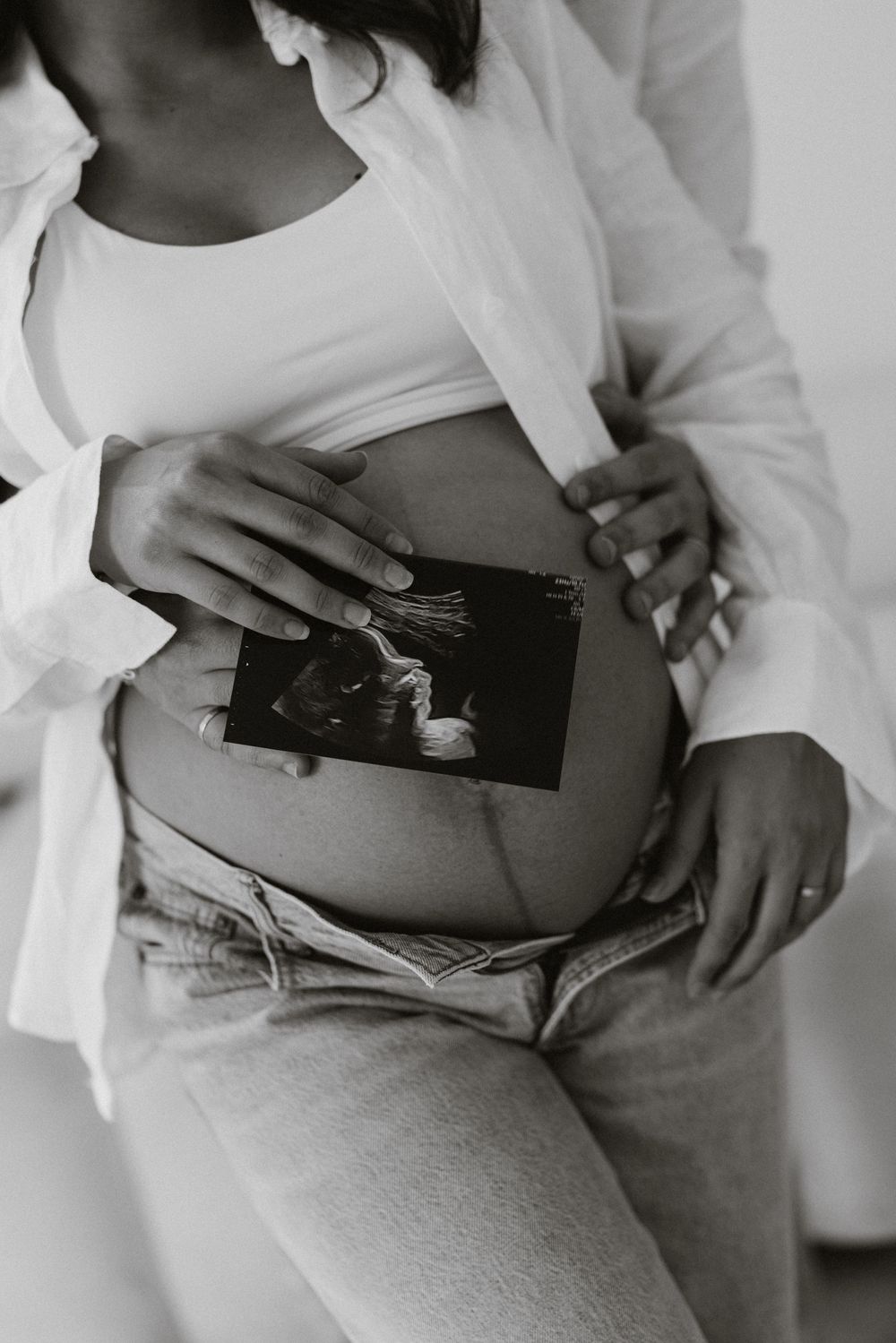 Black-and-white photo of an ultrasound image held against the belly at a maternity session.