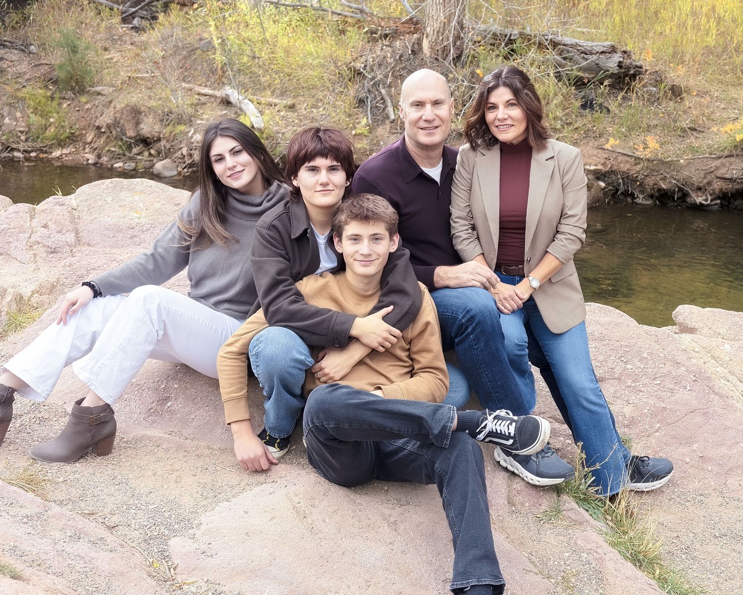A family sits together on rocks near a stream during an outdoor autumn photoshoot in nature.
