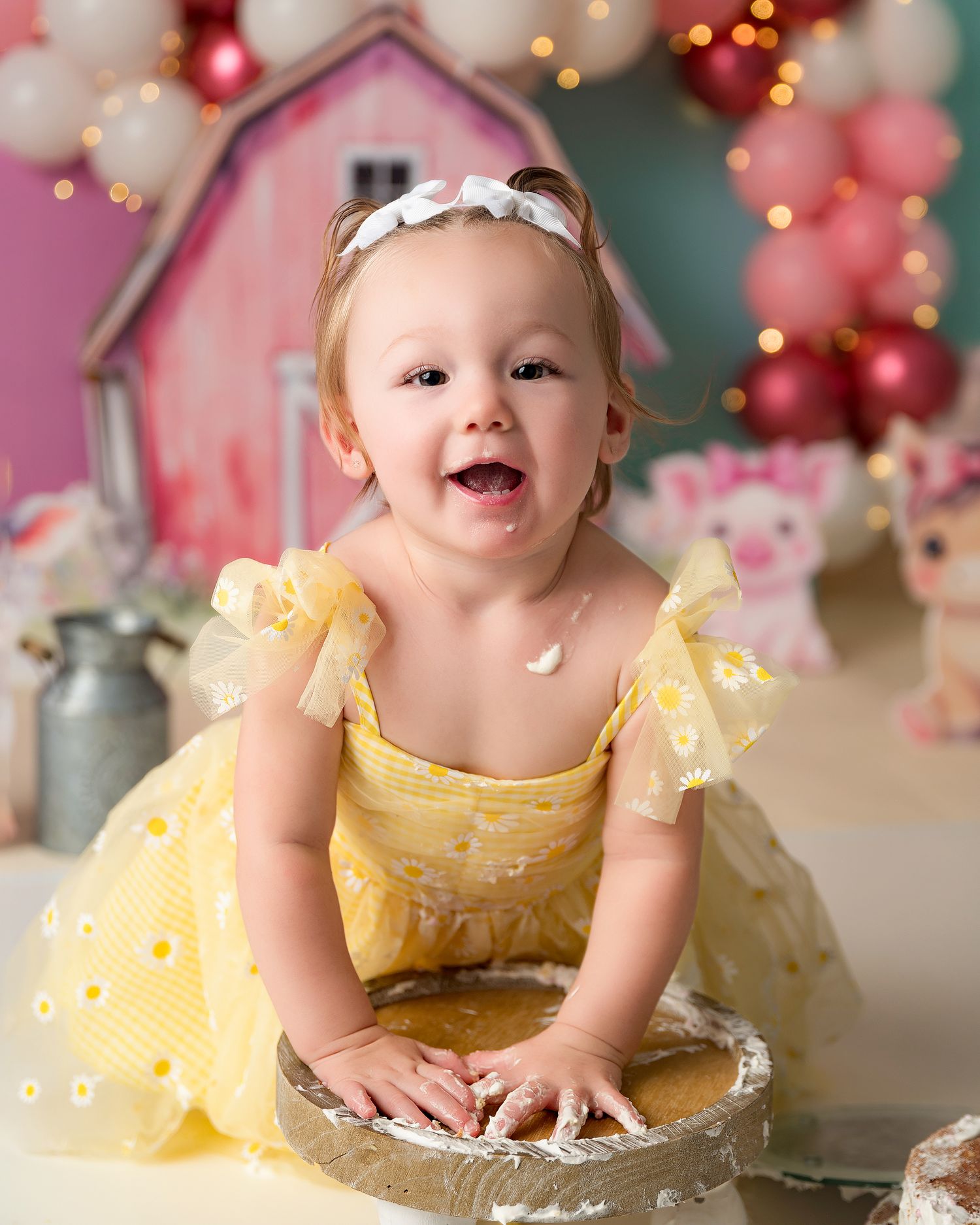 Baby in yellow dress smiles while sitting in vintage pie tin surrounded by pink and red holiday decorations.