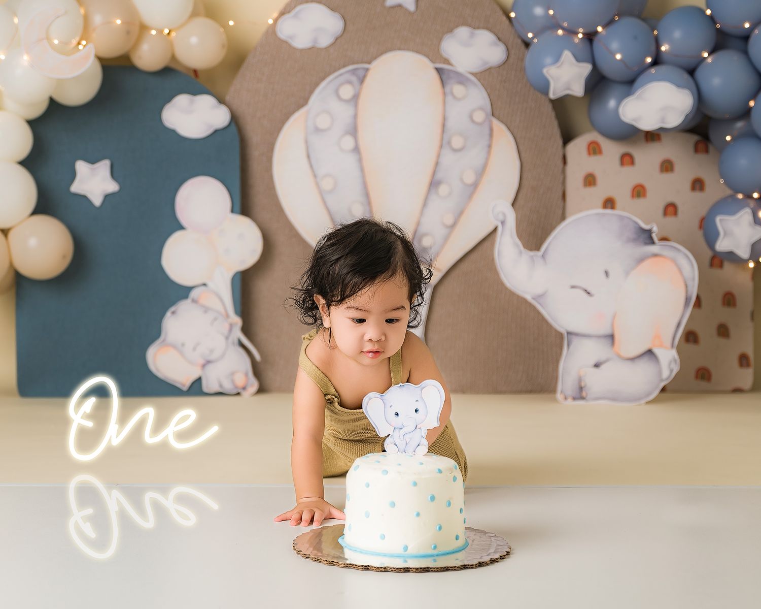 Sweet first birthday celebration with hot air balloon theme backdrop, white cake, and pastel balloon arch decorations.