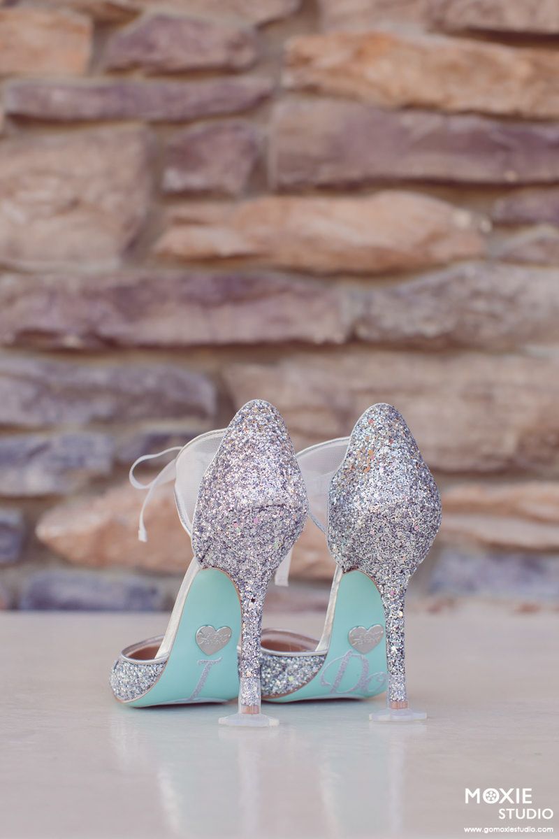 Elegant mint green and silver glitter wedding heels with sparkly embellishments against a rustic stone wall background.