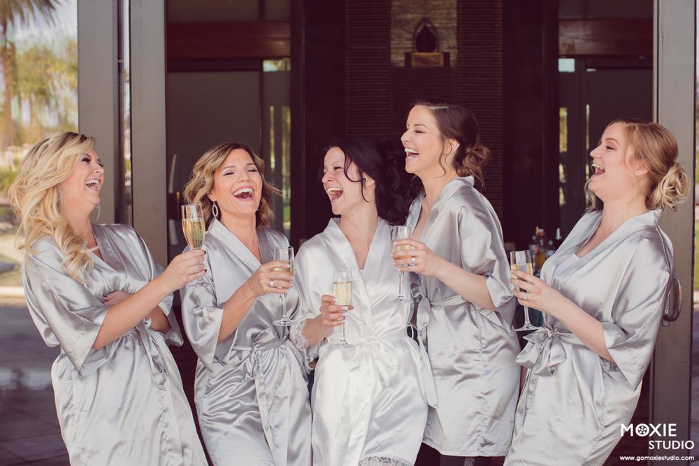 Wedding party in matching silver robes laughing and celebrating together with drinks.