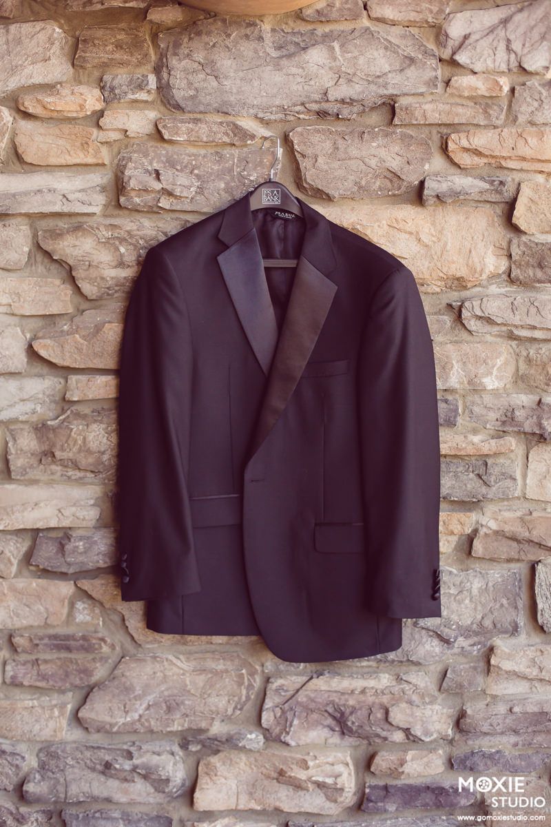 Black formal suit jacket hanging on stone wall for wedding preparation.
