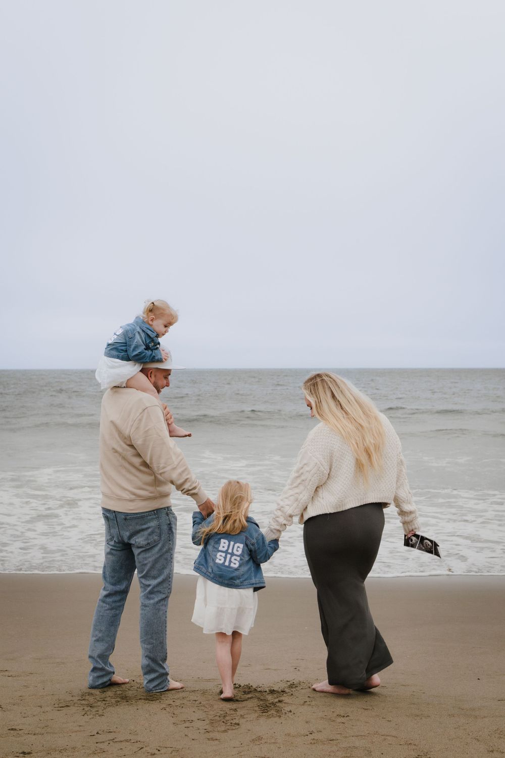 Family walks hand in hand along foggy beach shore looking at ocean waves.