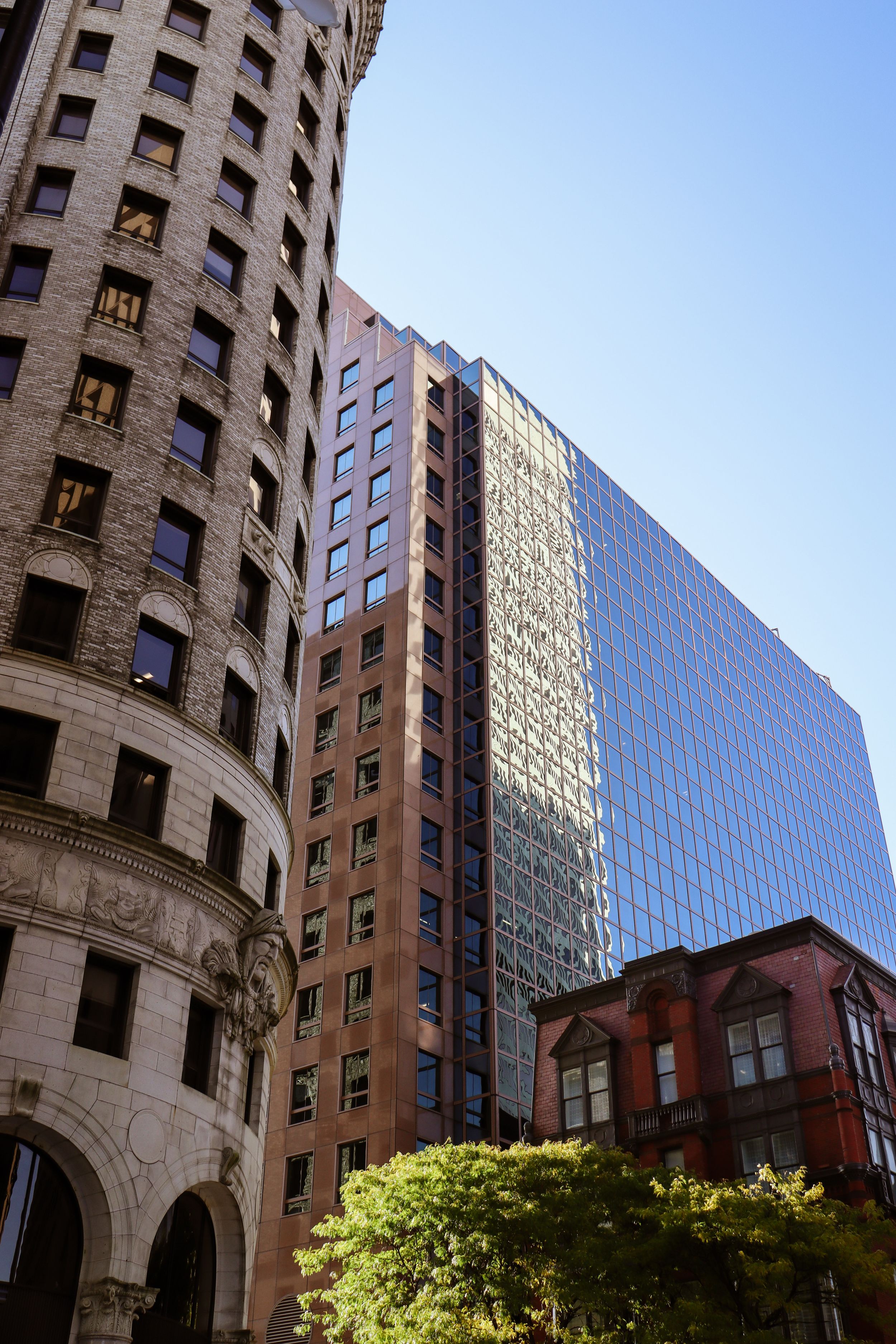 Modern glass and stone buildings stand against blue sky in an urban setting.
