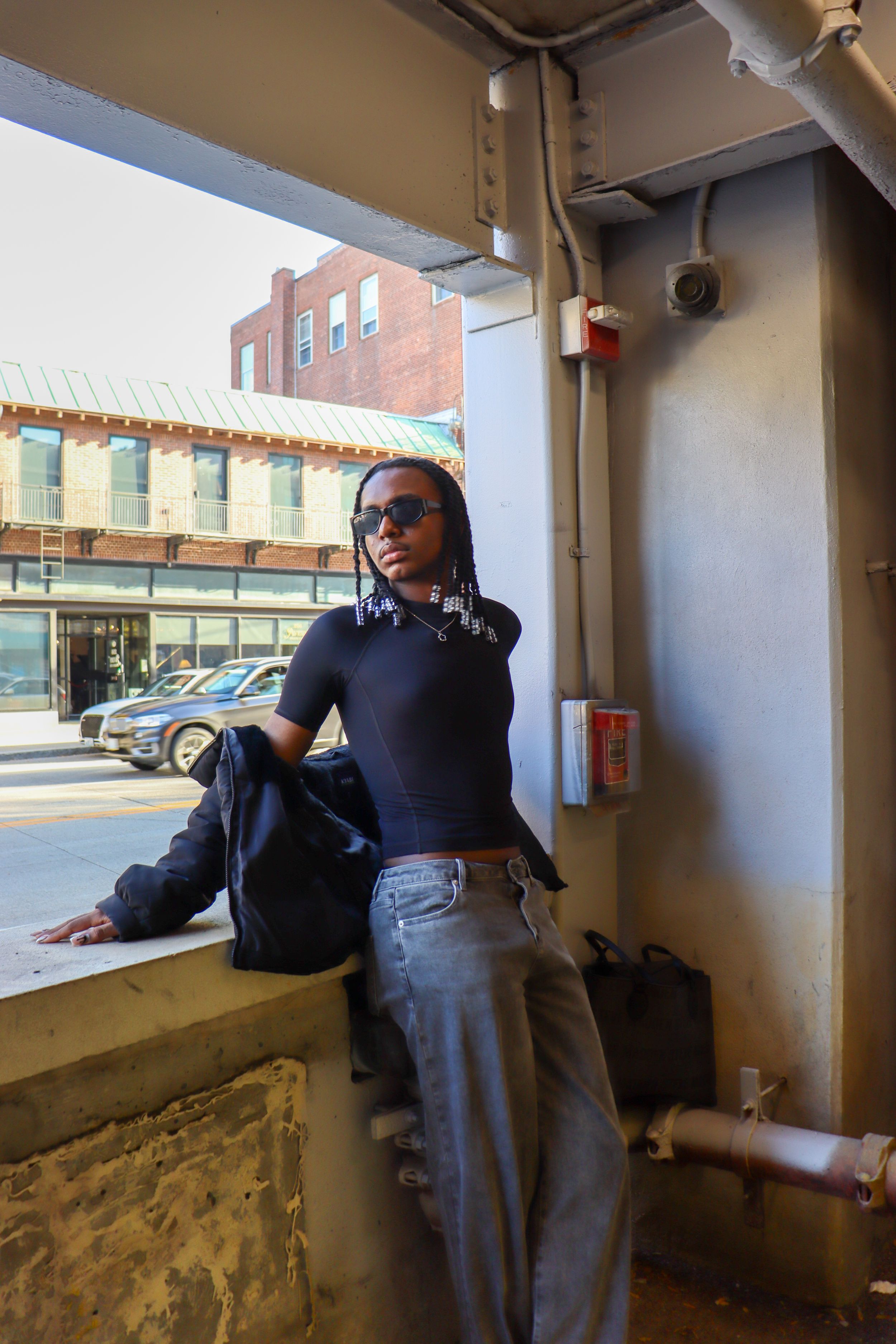 Person in casual attire leans against window ledge in urban setting with brick buildings visible.