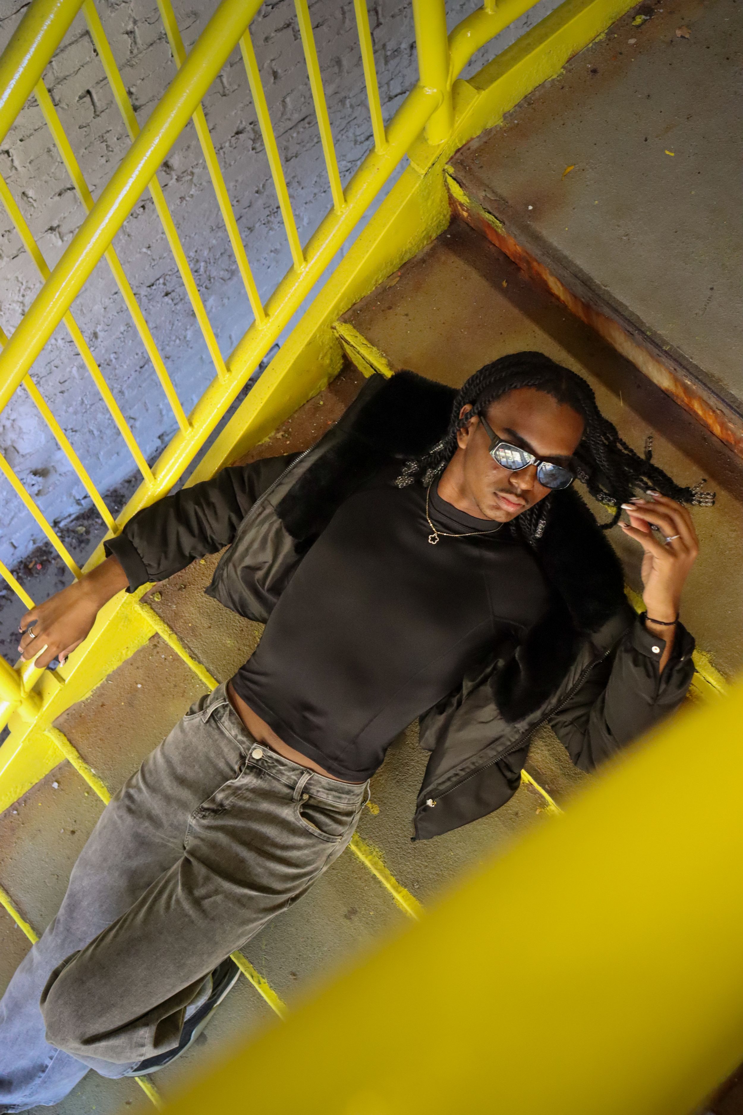 Stylish person in black attire posing in a stairwell with bright yellow railings.
