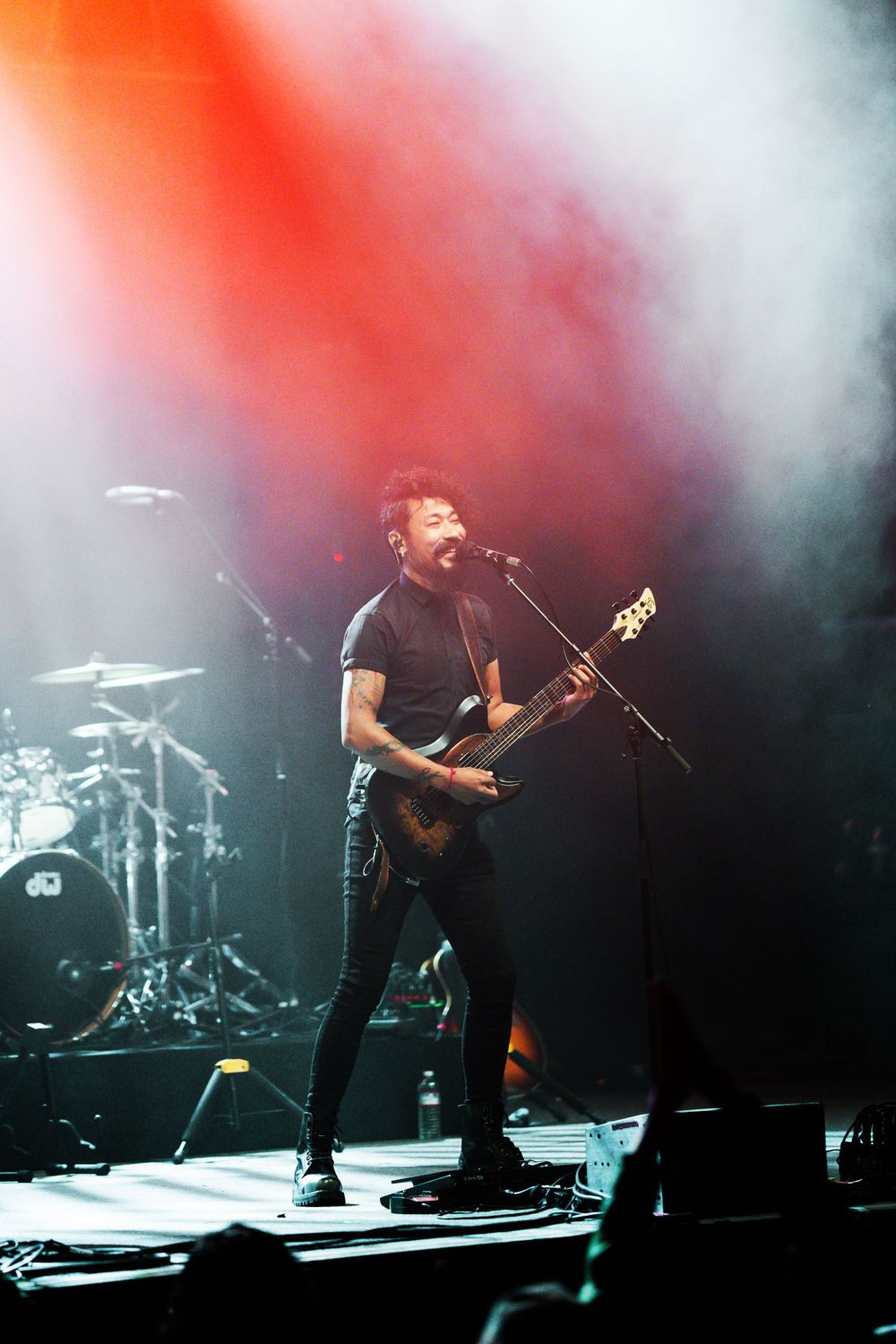 Musician performing on stage with guitar against dramatic red and white lighting.