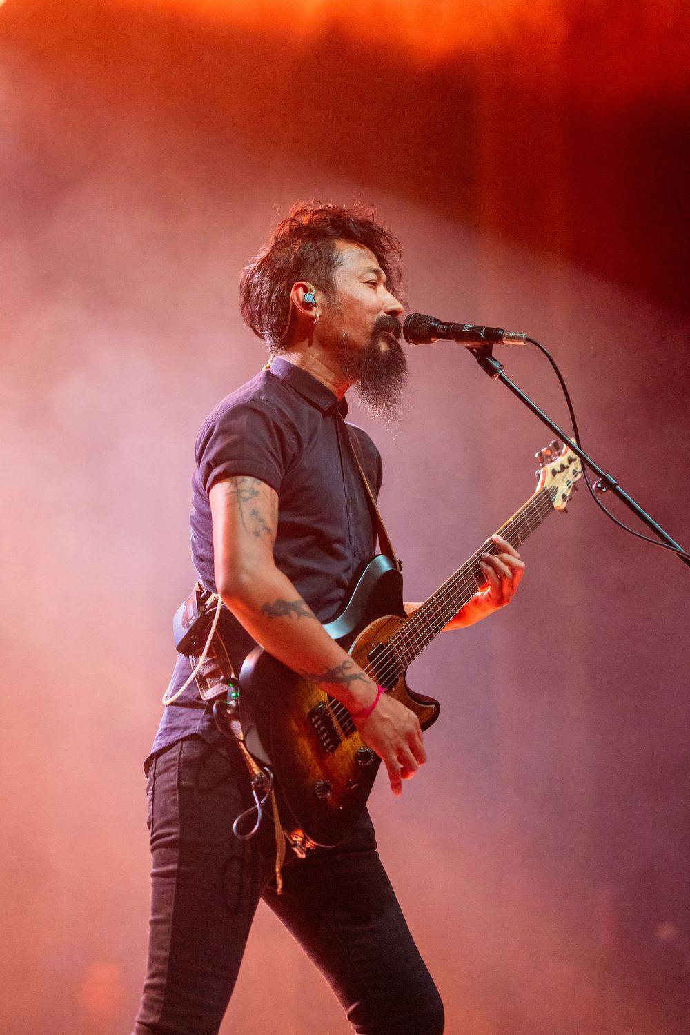 Guitarist in black shirt performs passionately on stage with red lighting.