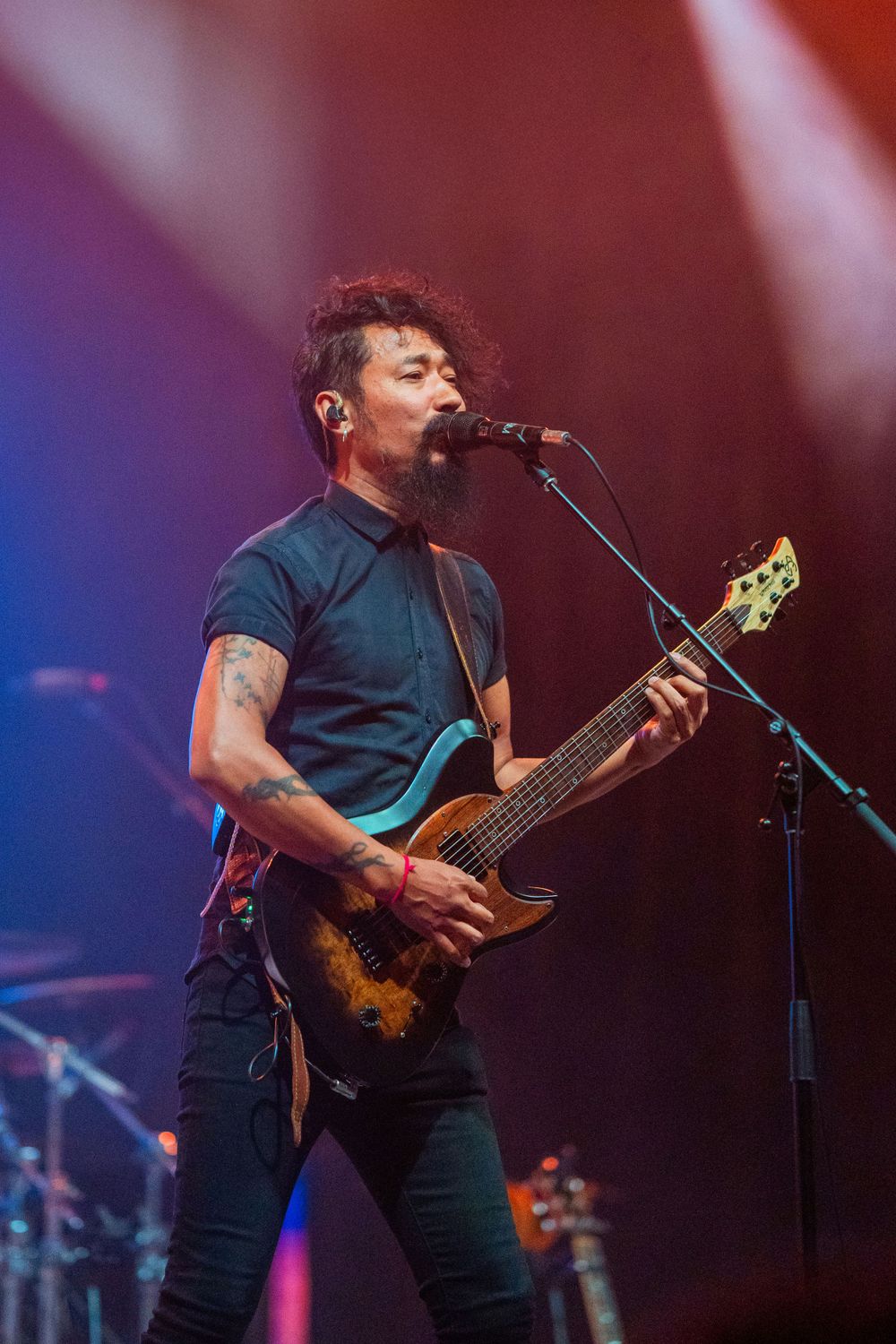 Rock musician plays guitar and sings into microphone with colorful stage lighting.