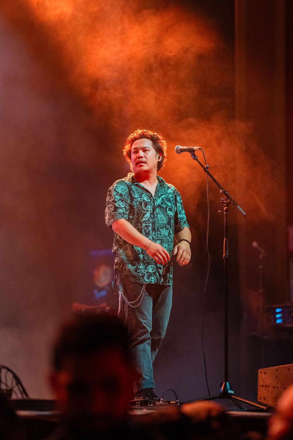 Singer performs on stage wearing patterned shirt with orange smoke effects.
