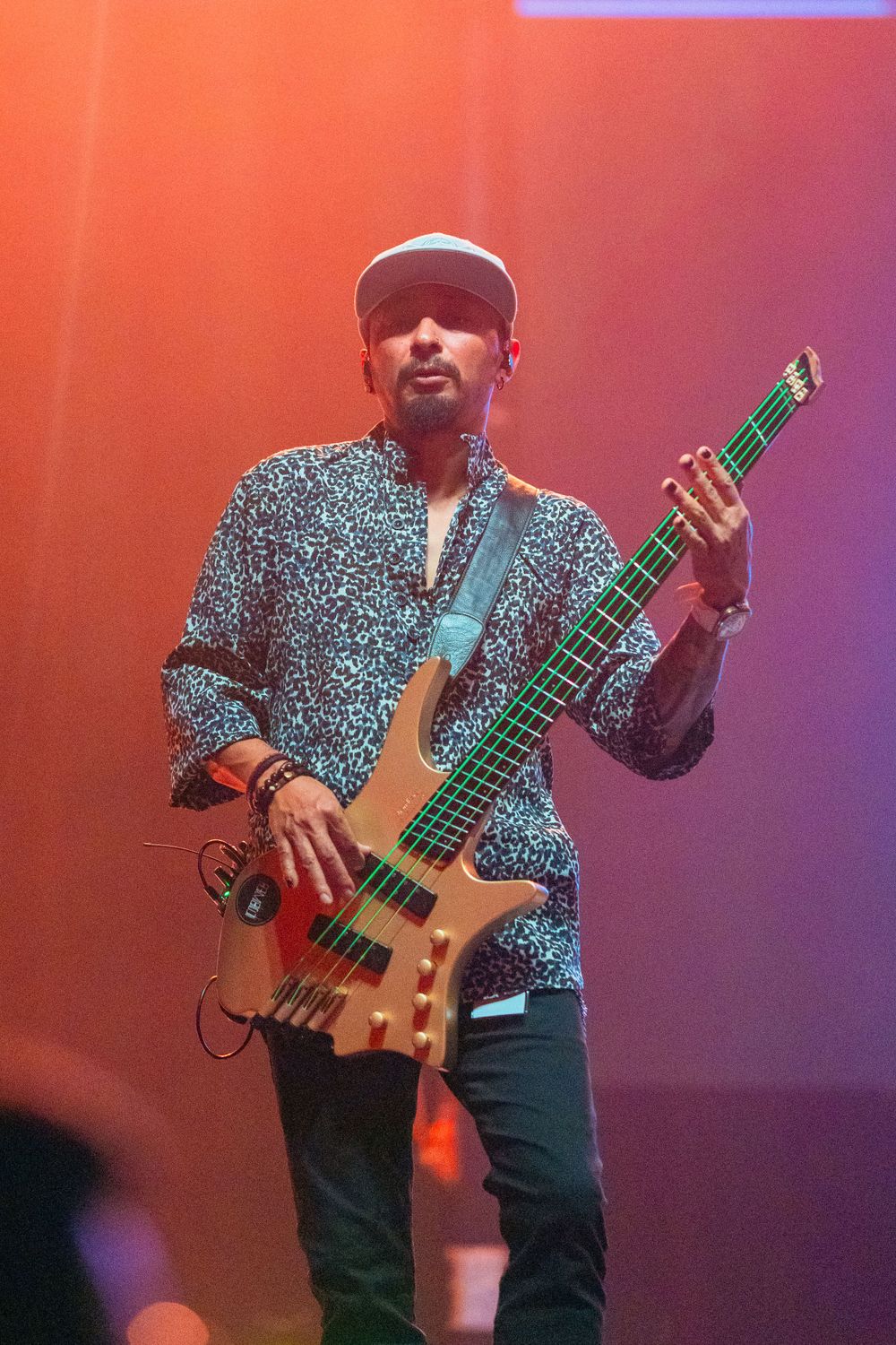 Bass player in patterned shirt performs with natural wood-colored bass guitar.