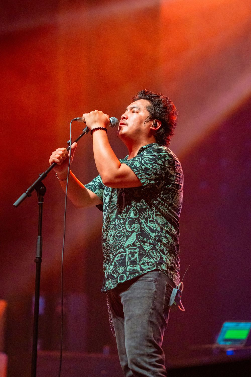 Singer in patterned shirt performs emotionally on stage with red lighting effects.
