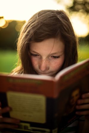Memphis Family Photographer portrait of girl reading at Shelby Farms during Golden Hour.