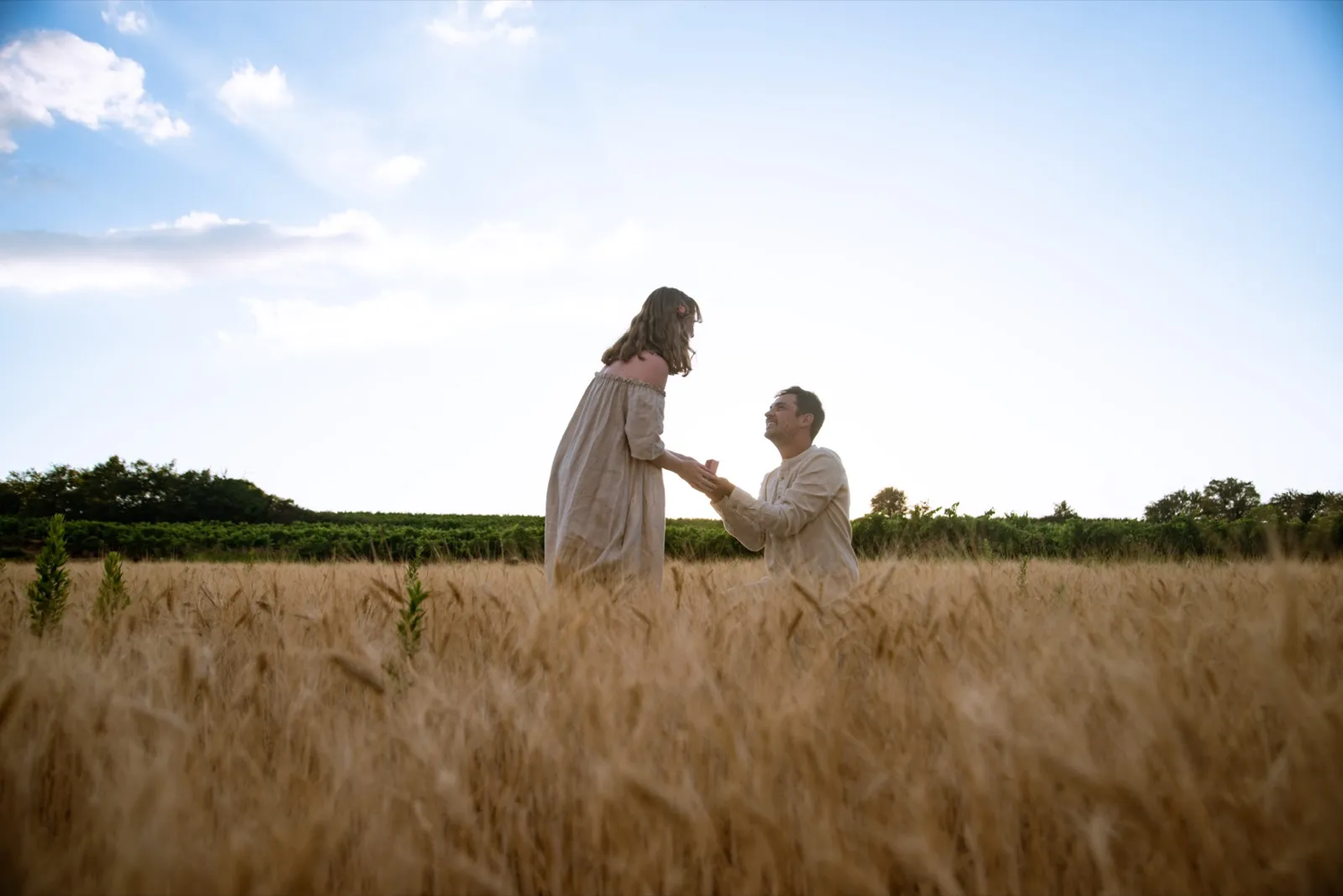 Un homme et une femme main dans la main dans un champ de blé doré, baignées par une lumière douce de fin de journée.