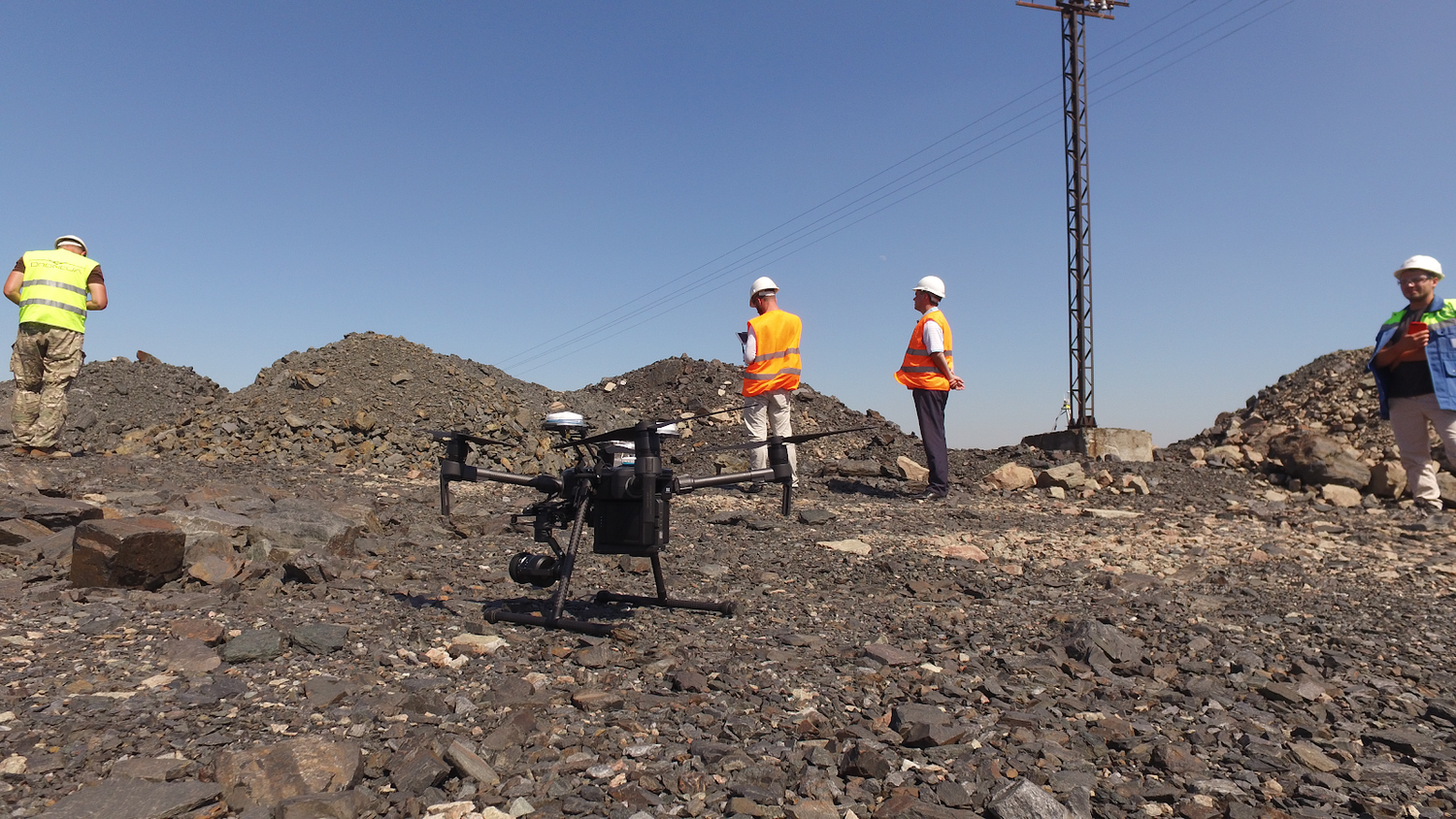 Survey team conducting drone operations on rocky terrain wearing safety gear.