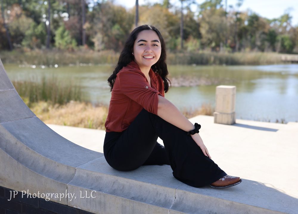 Outdoor portrait by a lake with person in rust-colored top sitting on curved surface.