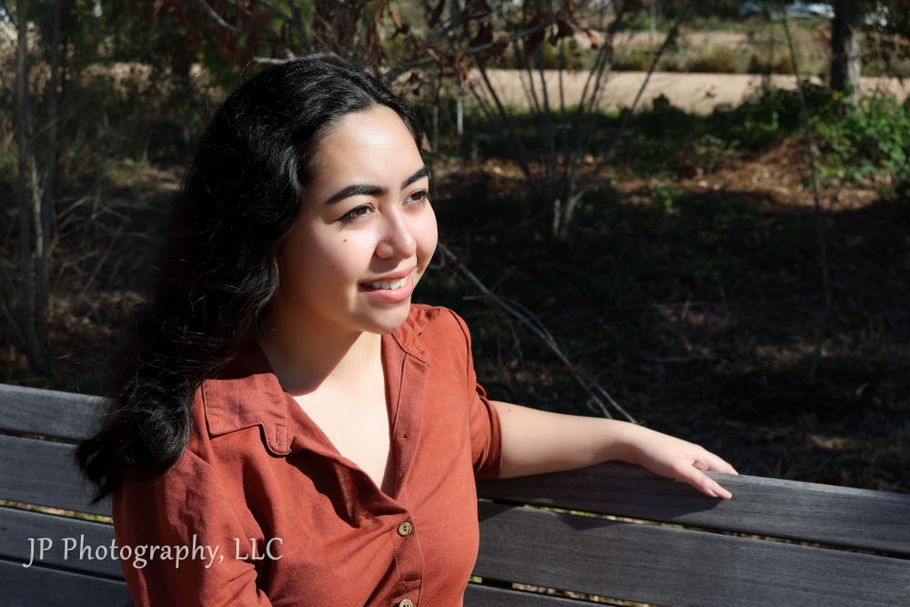 Sunny outdoor portrait on bench with person wearing coral button-up shirt.