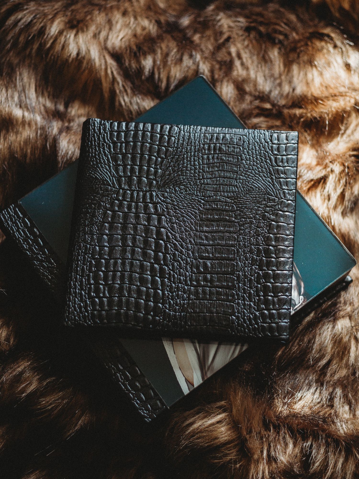 Stylish black crocodile pattern leather wallet photographed on brown fur texture background.