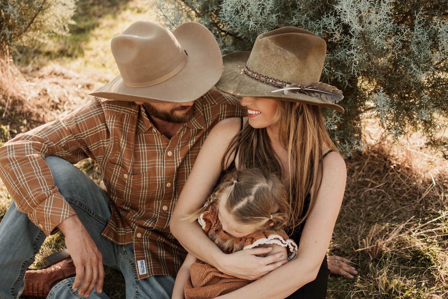 A couple in western attire share intimate moments in a sunlit outdoor setting with a rustic atmosphere.