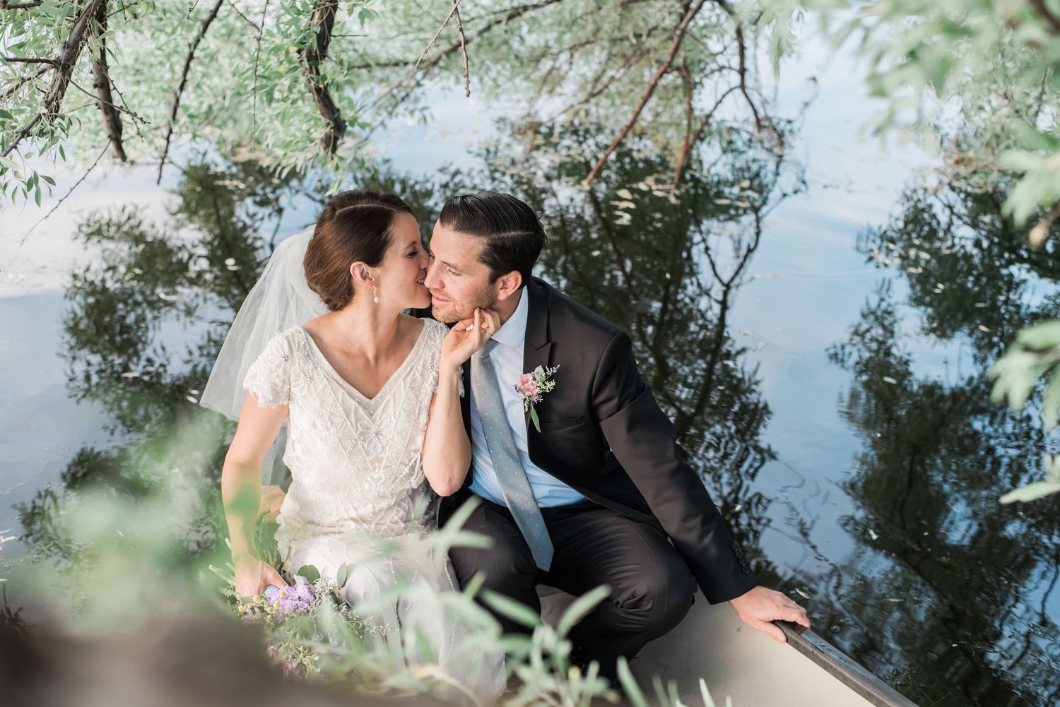 Couple in formal attire walking together on a grassy lawn surrounded by evergreen trees and landscaping.