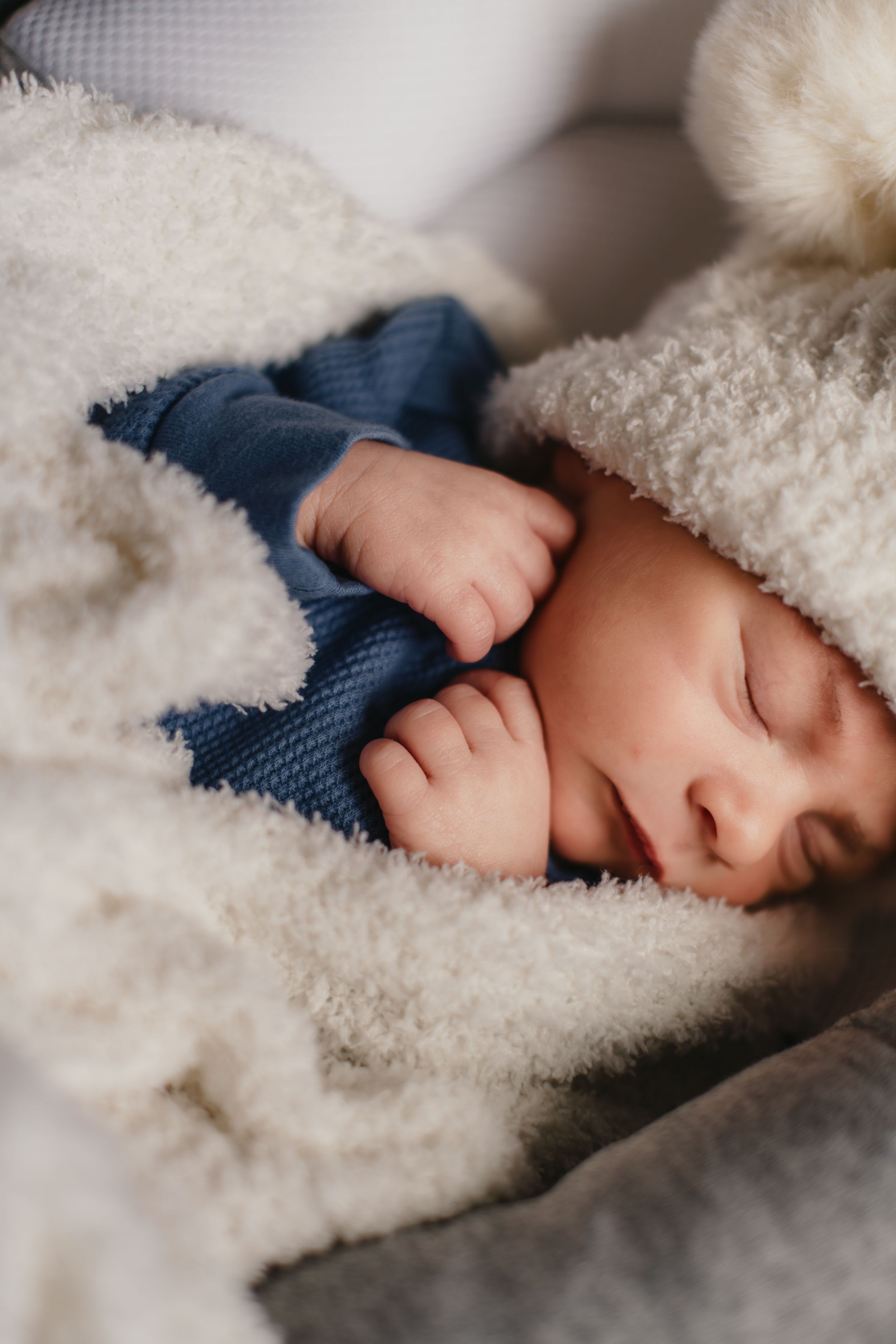 Newborn baby sleeping peacefully in cozy white blanket and blue outfit.