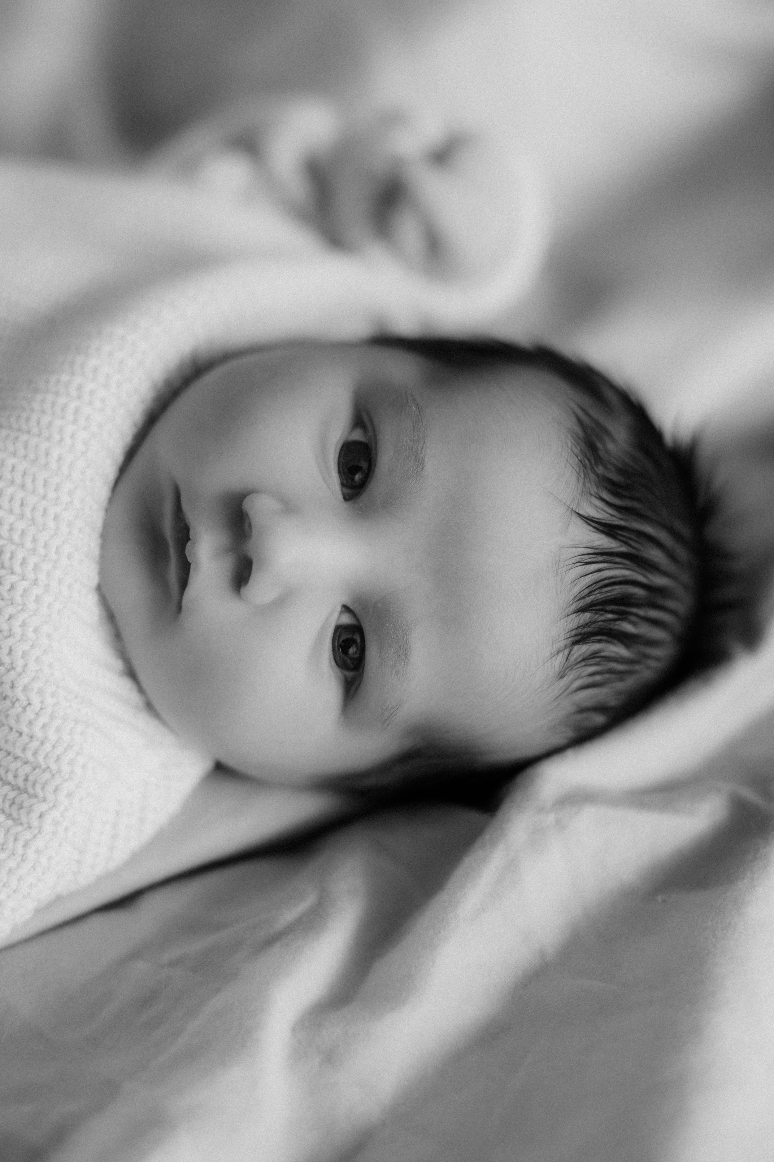 Close up black and white portrait of an infant in soft white blankets.