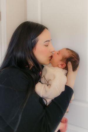 Intimate portrait of parent giving newborn in white sweater a gentle kiss.
