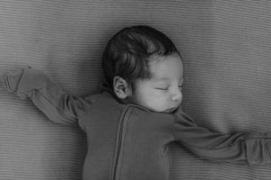 A sleeping infant lies peacefully on gray fabric while wearing a long-sleeved top in black and white.