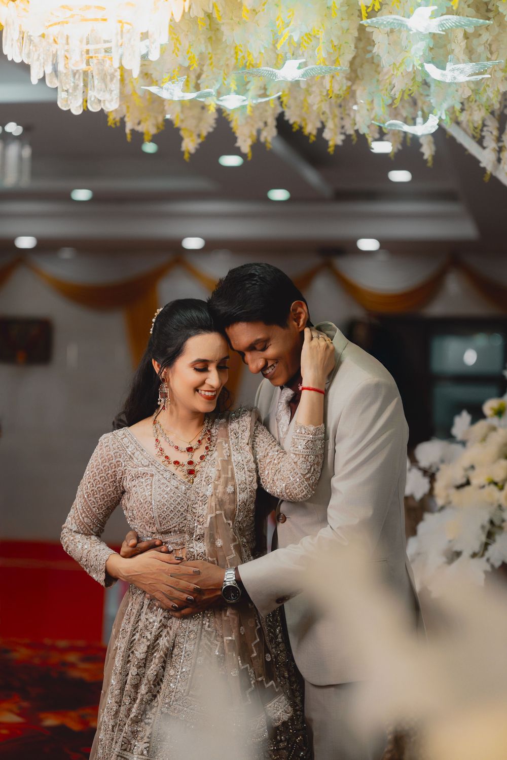 A couple shares intimate moments during a wedding reception under elegant crystal chandeliers and floral decor.