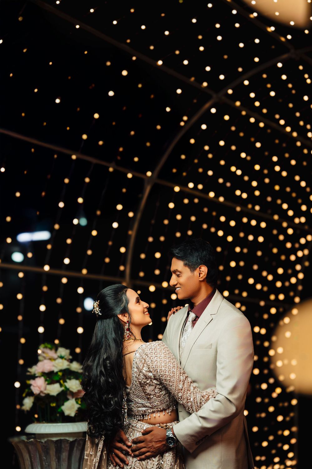 Romantic couple pose in front of a twinkling light backdrop during their wedding celebration.