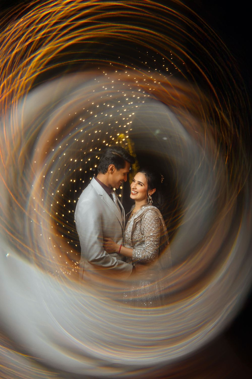 A couple embraces in a romantic swirling golden light effect creating a dreamy spiral motion blur atmosphere.