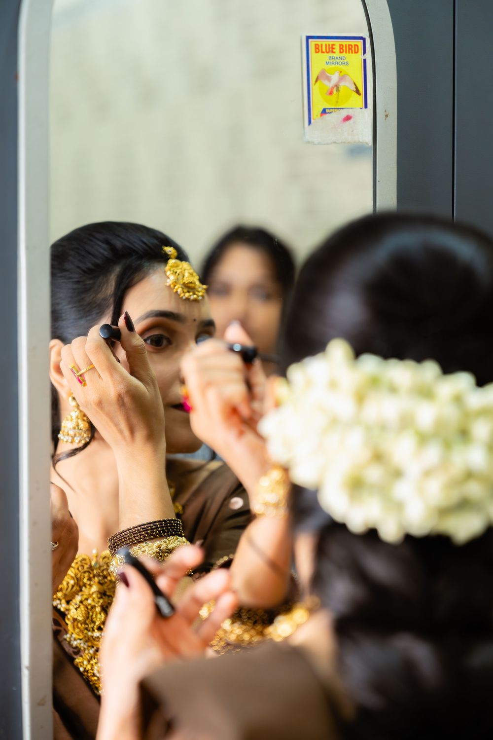 Reflections of a bridal party applying makeup in multiple mirrors during wedding preparations.