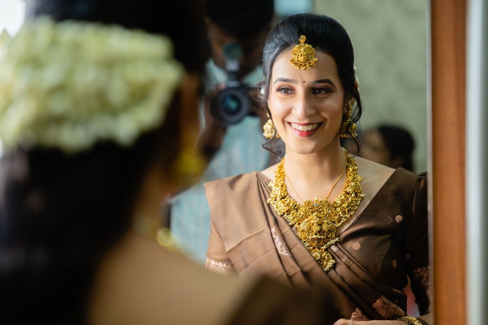A bride in traditional Indian wedding attire and gold jewelry smiles while getting ready for her wedding ceremony.