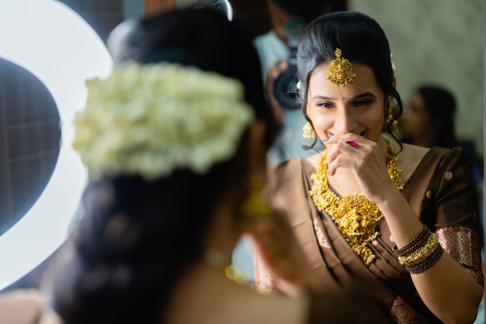 Someone in elaborate gold South Asian jewelry and brown attire is reflected in a mirror while getting ready.