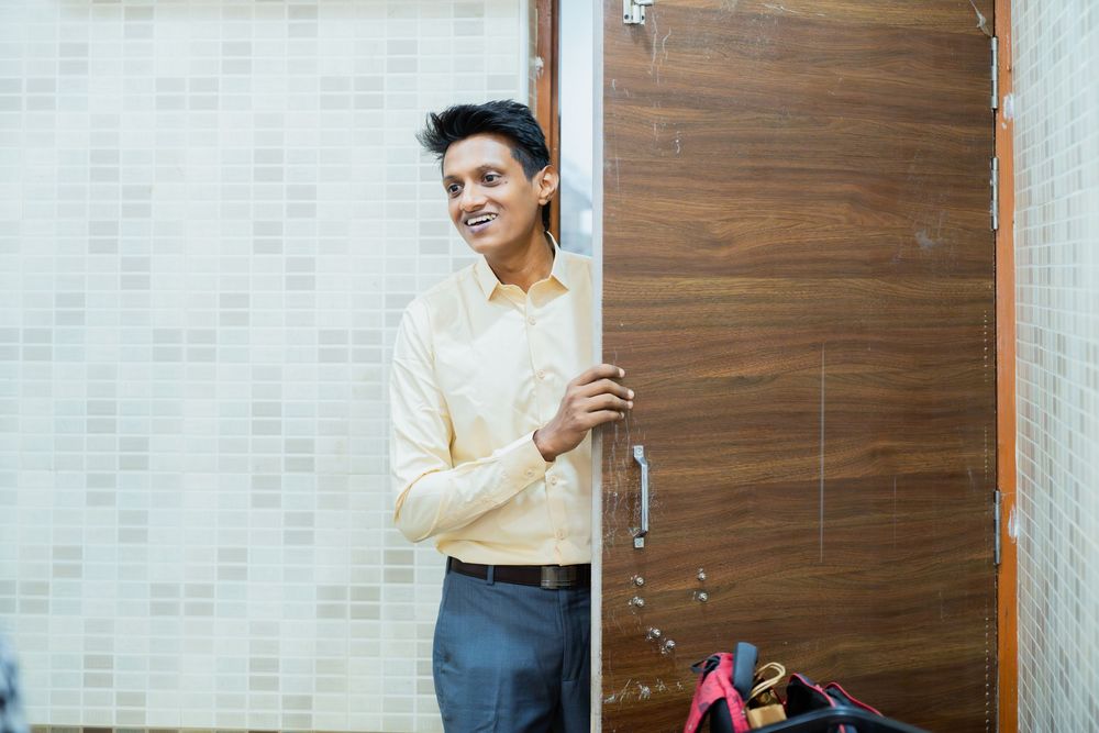 Person in casual attire stands playfully near a wooden door in an interior hallway.
