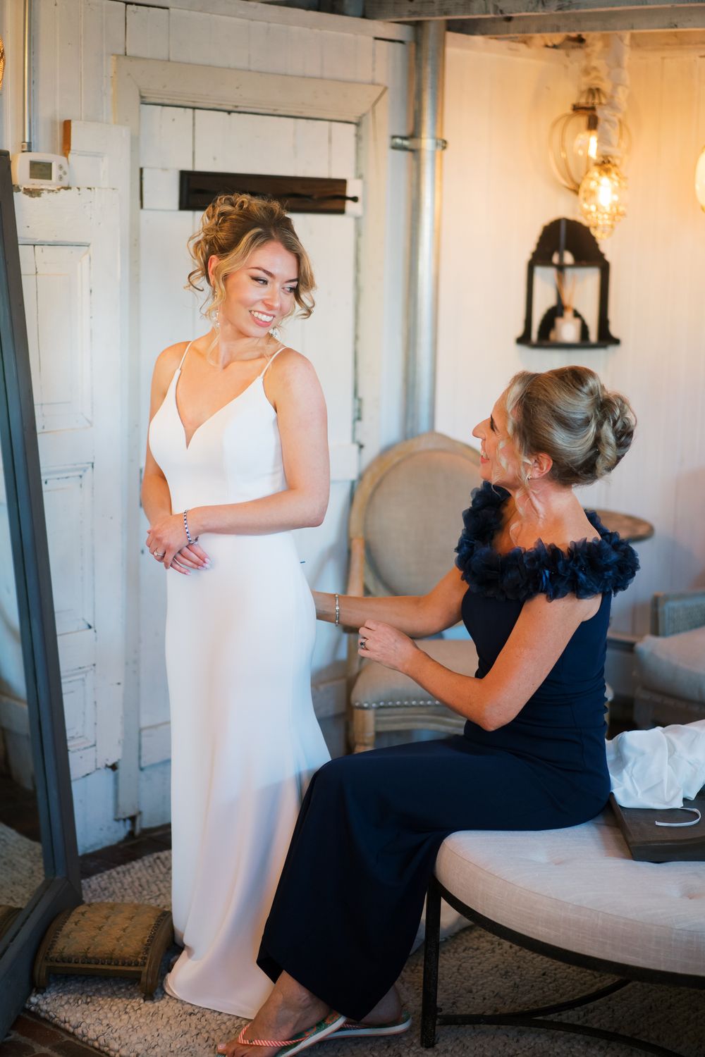Two attendants in contrasting white and navy dresses share an emotional moment during wedding preparations.