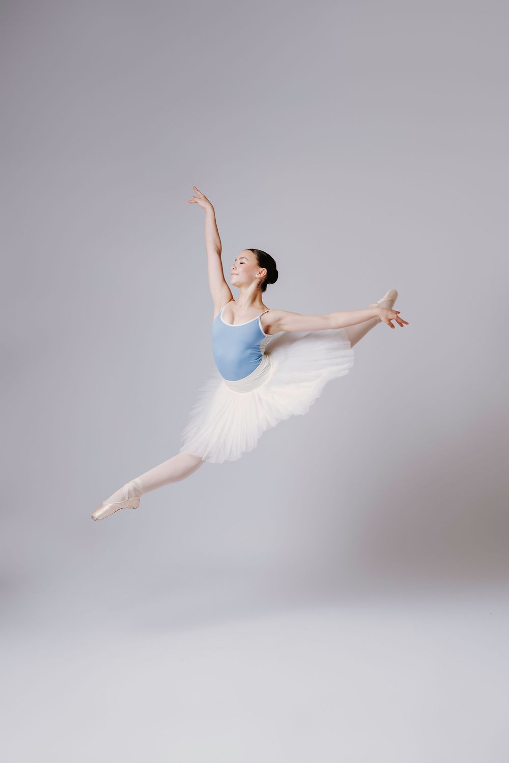 Ballet dancer in classical tutu executes dynamic leaping movements in a minimalist studio setting.