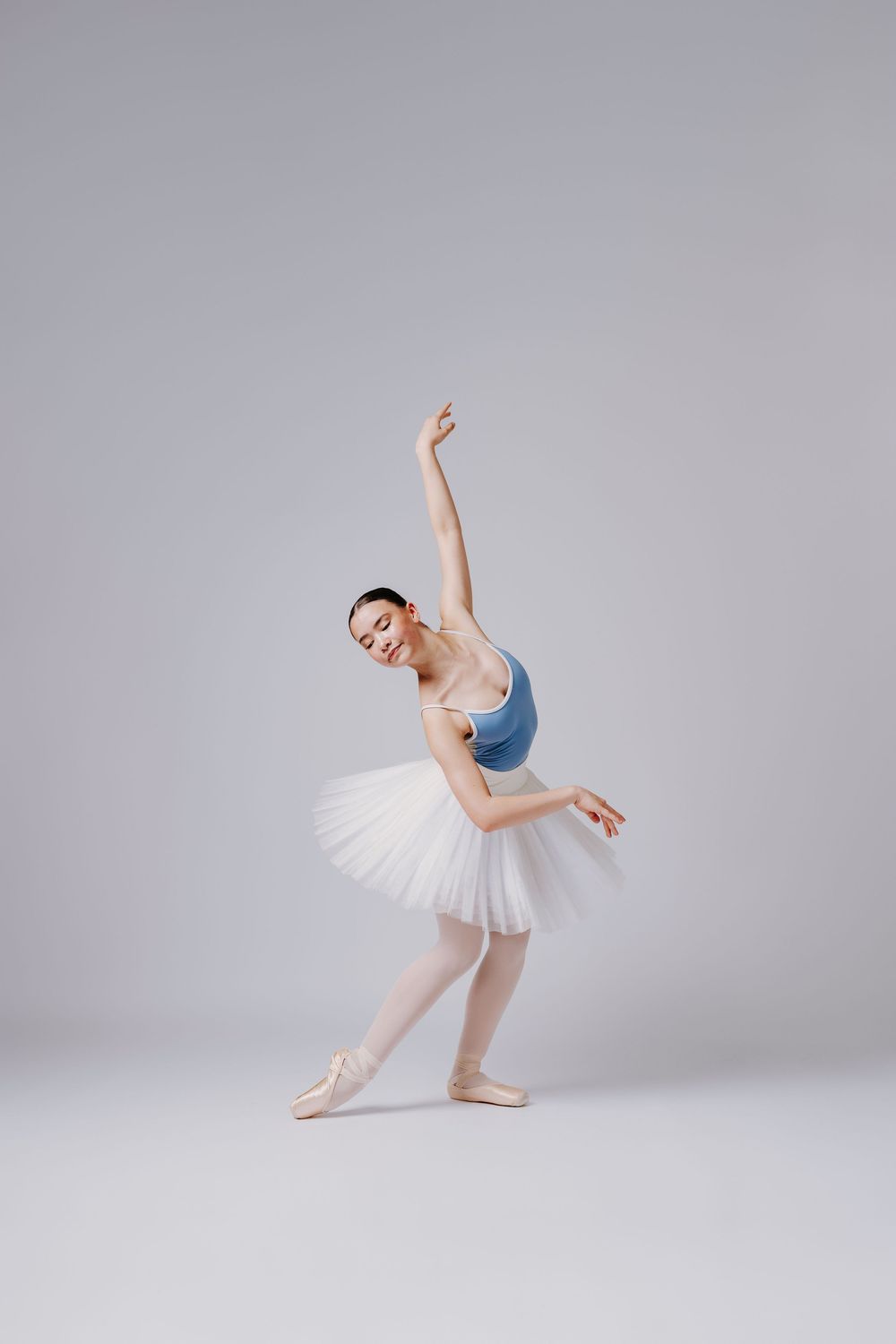 Graceful ballet dancer in white tutu and blue leotard performs elegant poses in bright studio setting.