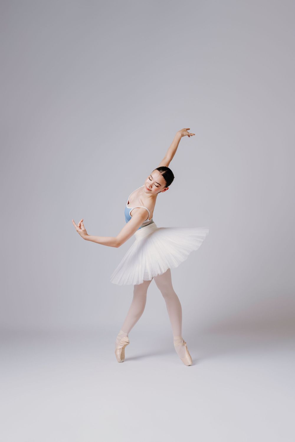 Elegant ballet dancer in white tutu performing graceful poses against light gray studio background.