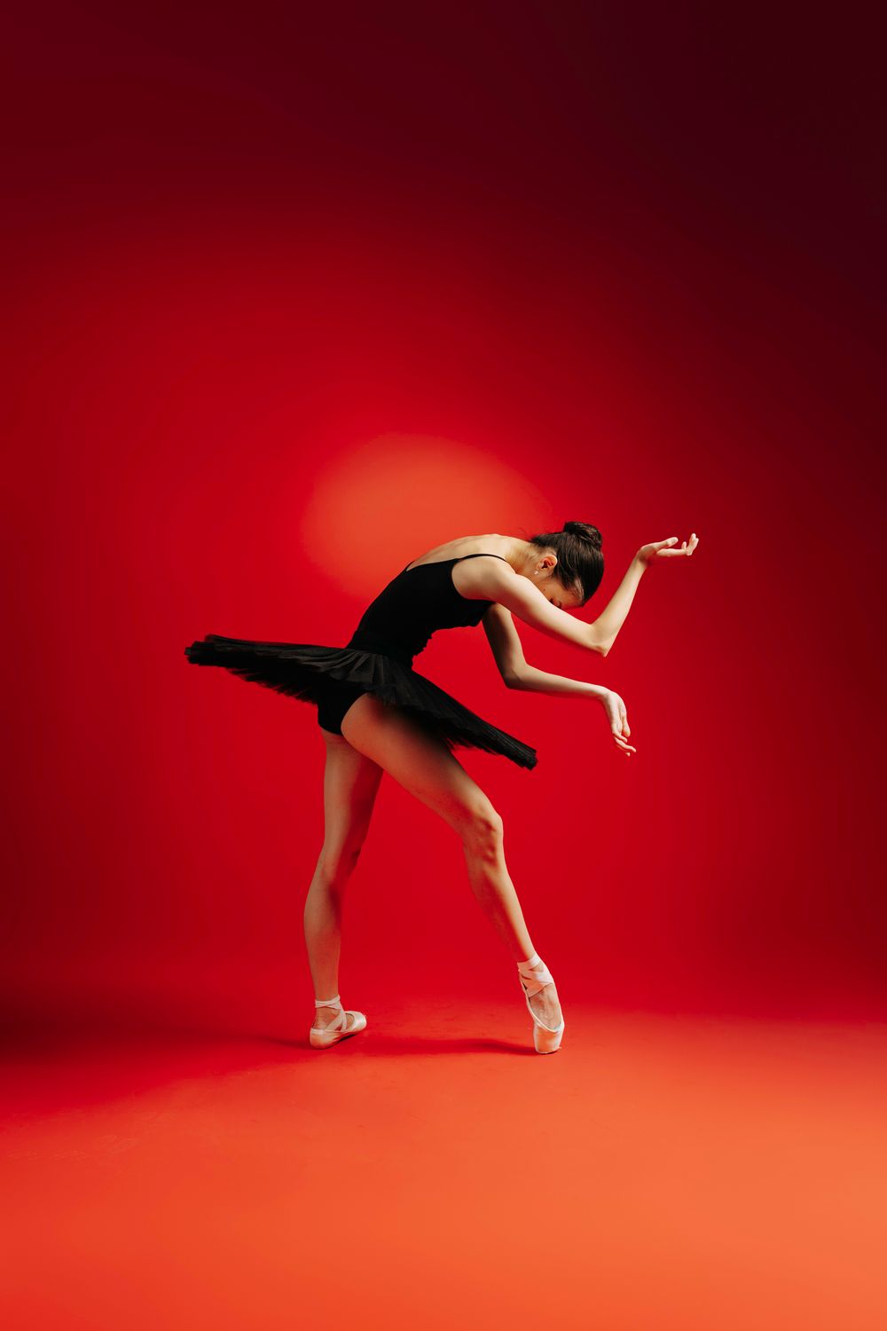 Graceful ballet dancer in black tutu performs elegant pose en pointe against red backdrop.
