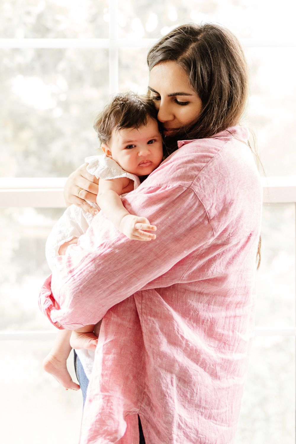 Mother holds her baby in front of a bright window during her in-home Bay Area newborn session with Cindy Tucey Photography