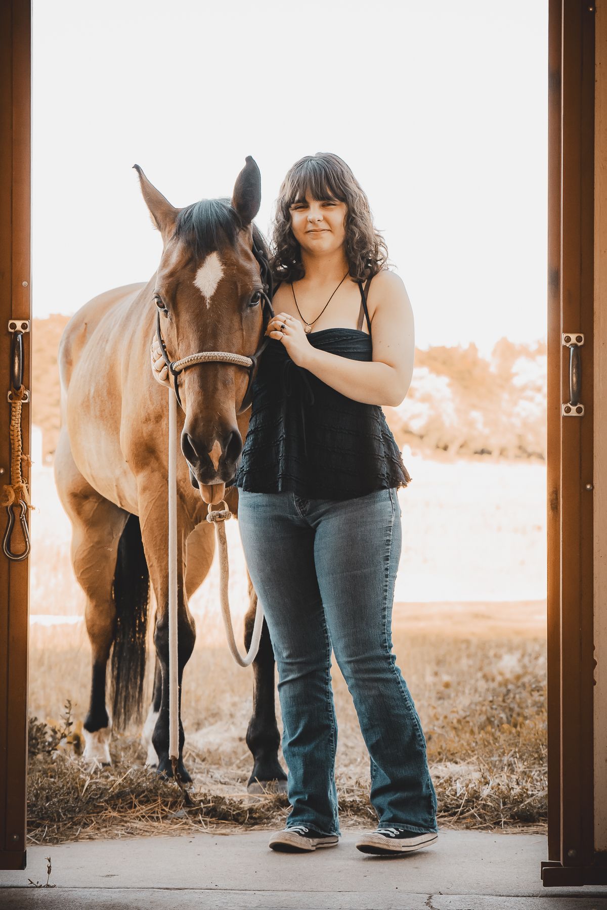 Horses and handler silhouetted in a barn entrance during sunset.