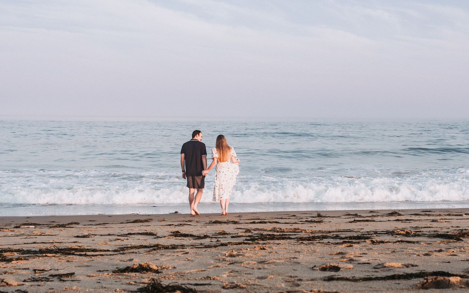 Ocean waves crash on sandy beach as couple strolls along shoreline at sunset creating peaceful coastal scene.