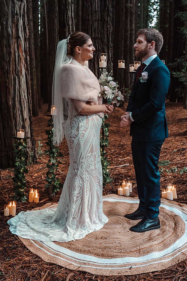 Couple shares intimate first dance surrounded by lit candles on circular platform in enchanting redwood forest setting.