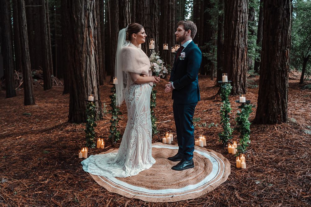 A wedding ceremony in a redwood forest with a circular rug and glowing candles creating an intimate woodland setting.